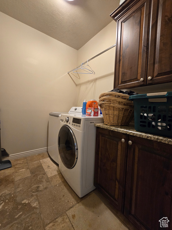 Clothes washing area featuring cabinet space, stone finish flooring, a textured ceiling, washer and dryer, and baseboards