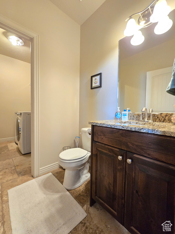 Half bathroom featuring stone tile flooring, toilet, washing machine and dryer, vanity, and baseboards