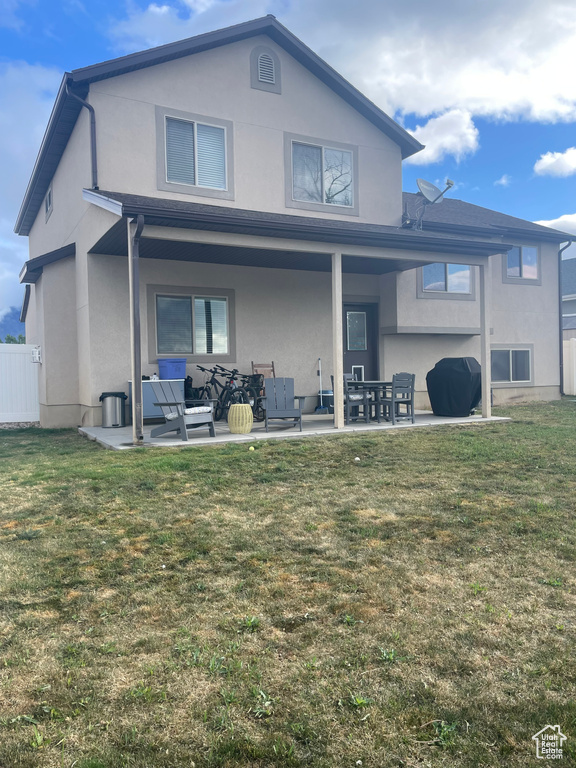 Back of house featuring stucco siding, fence, a lawn, and a patio