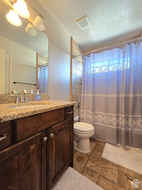 Full bathroom with visible vents, toilet, vanity, a textured ceiling, and stone tile flooring