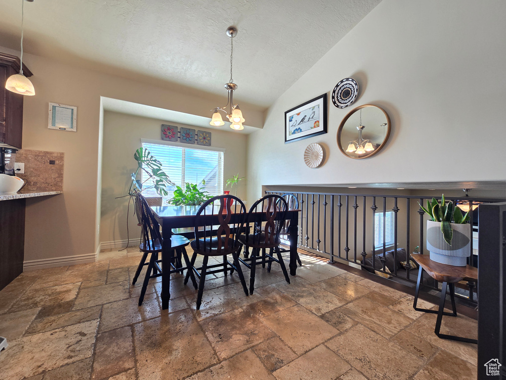 Dining room with a textured ceiling, high vaulted ceiling, a notable chandelier, baseboards, and stone tile flooring