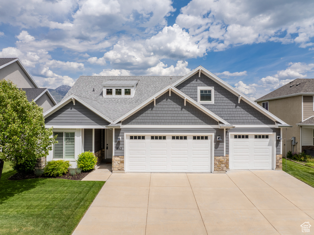 Craftsman house with stone siding, driveway, a front lawn, and a shingled roof