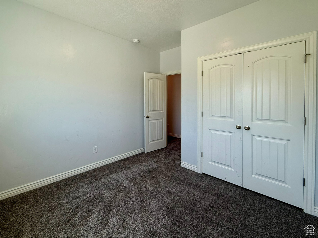 Unfurnished bedroom featuring dark carpet, baseboards, and a closet