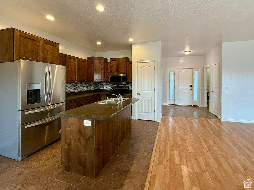 Kitchen with dark countertops, tasteful backsplash, an island with sink, appliances with stainless steel finishes, and a sink
