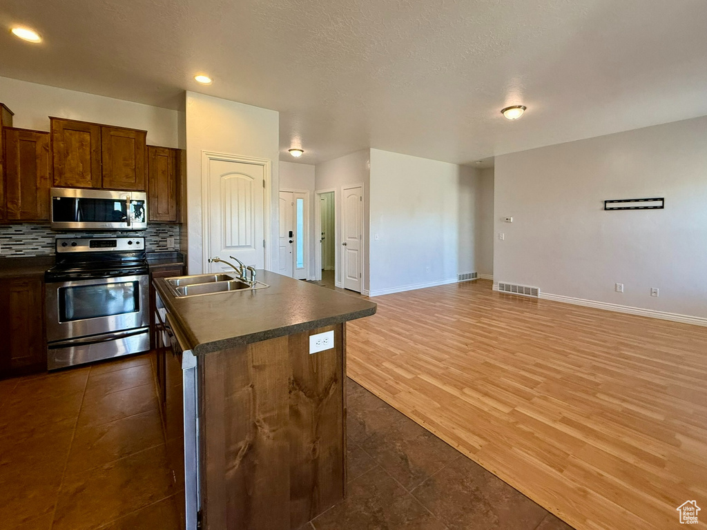 Kitchen featuring stainless steel appliances, a sink, dark countertops, tasteful backsplash, and an island with sink