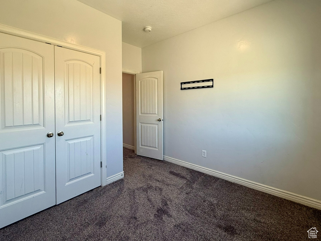 Unfurnished bedroom featuring dark colored carpet, baseboards, and a closet