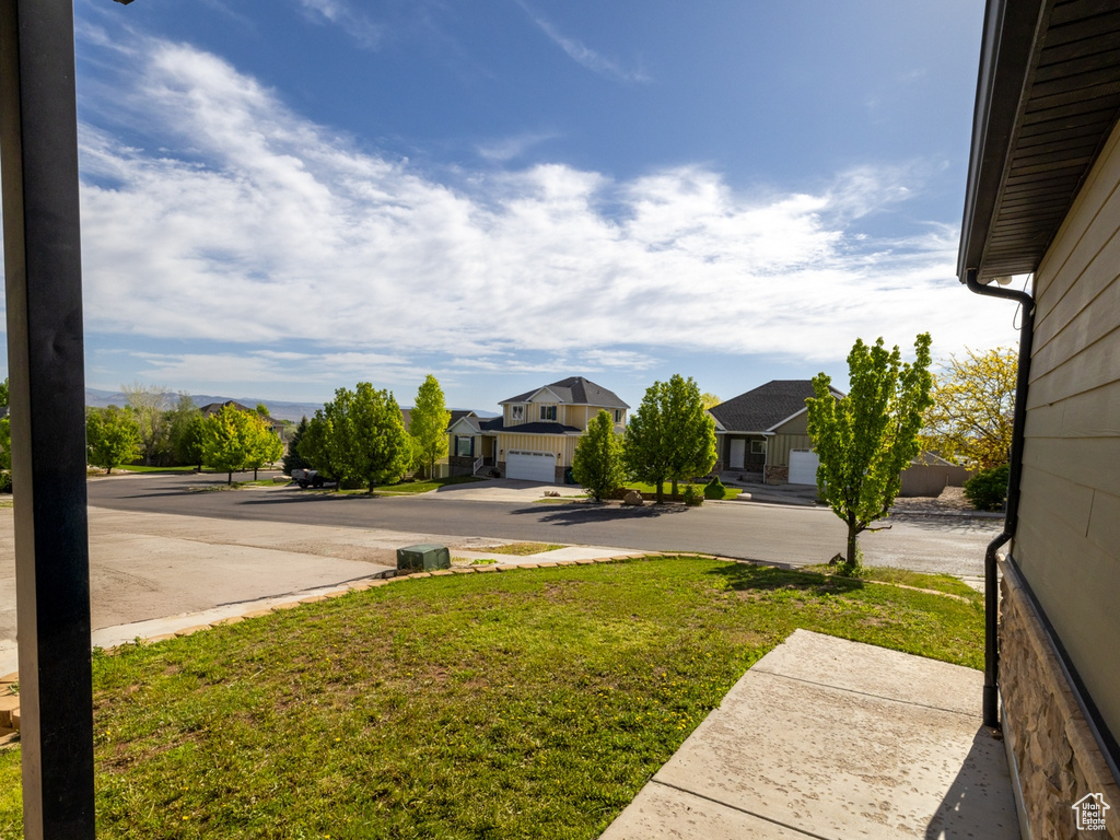 View of green lawn with a residential view, concrete driveway, and a garage