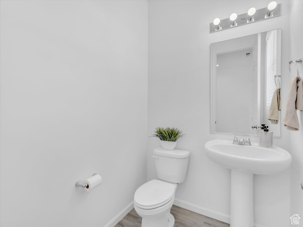 Half bath with a sink, wood finished floors, toilet, and baseboards