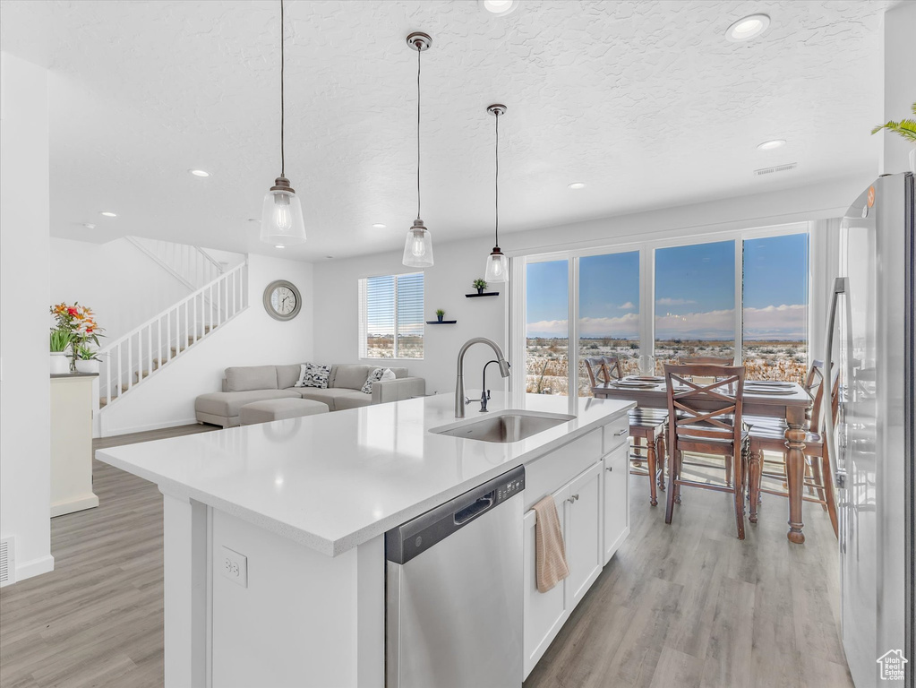 Kitchen with decorative light fixtures, freestanding refrigerator, light countertops, stainless steel dishwasher, and a sink