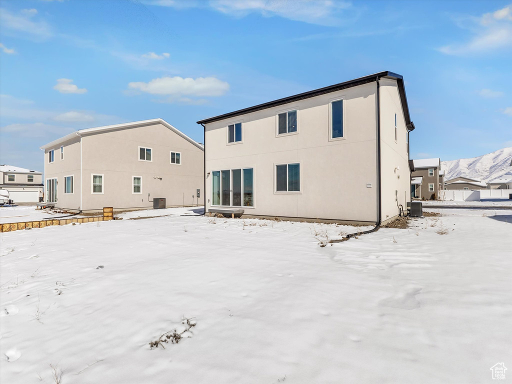 Snow covered back of property featuring central AC unit and stucco siding