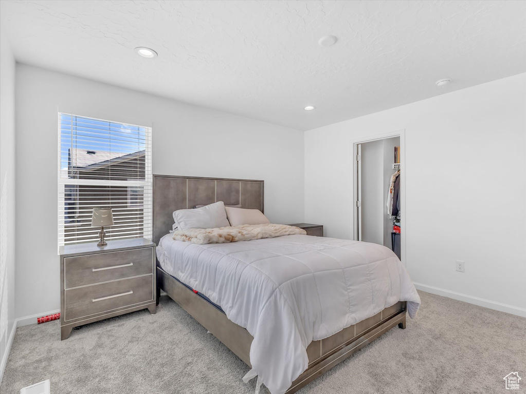 Bedroom with baseboards, light colored carpet, a walk in closet, a closet, and recessed lighting