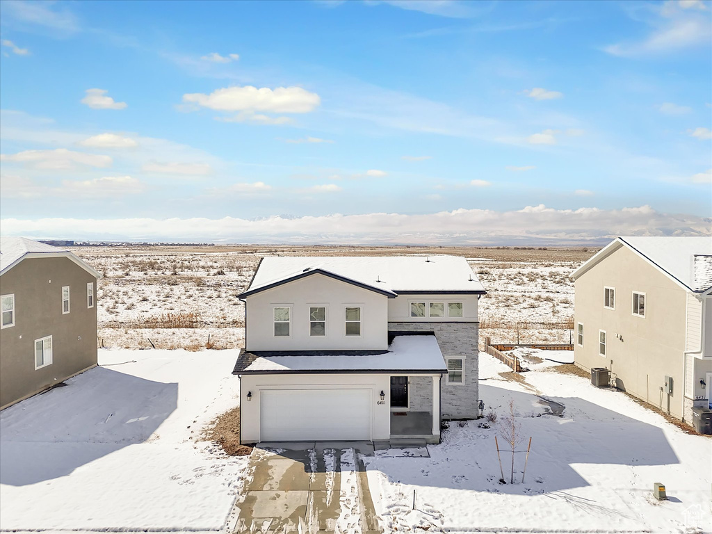 Snow covered rear of property featuring a garage, central air condition unit, and stucco siding