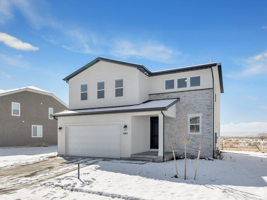 View of front of home featuring a garage, stone siding, and stucco siding