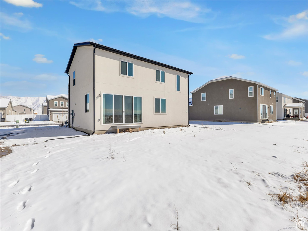 Snow covered rear of property featuring a residential view and stucco siding