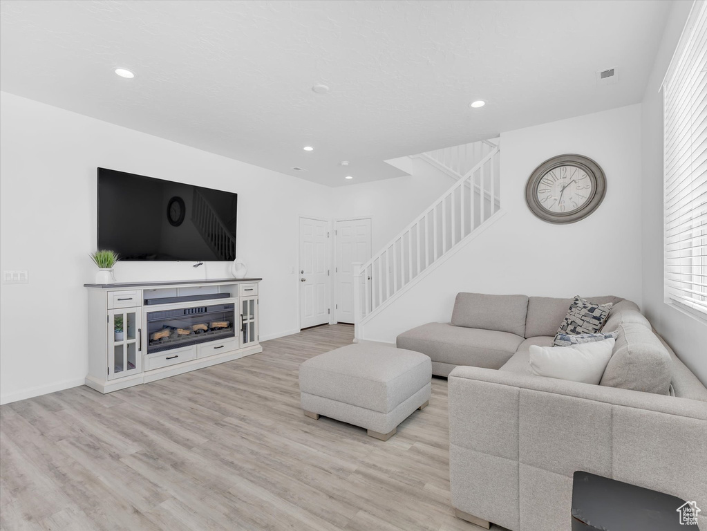 Living room with a glass covered fireplace, stairway, light wood finished floors, and recessed lighting