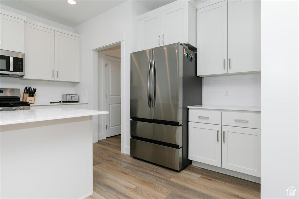 Kitchen featuring white cabinets, light wood-type flooring, appliances with stainless steel finishes, and backsplash