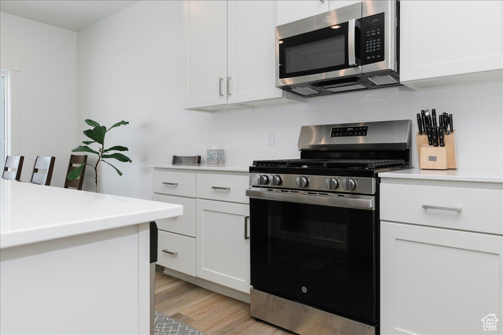 Kitchen featuring appliances with stainless steel finishes, light wood-type flooring, white cabinetry, and backsplash