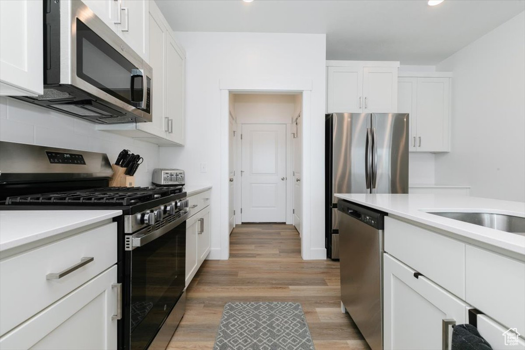 Kitchen featuring decorative backsplash, appliances with stainless steel finishes, white cabinets, and light hardwood / wood-style floors