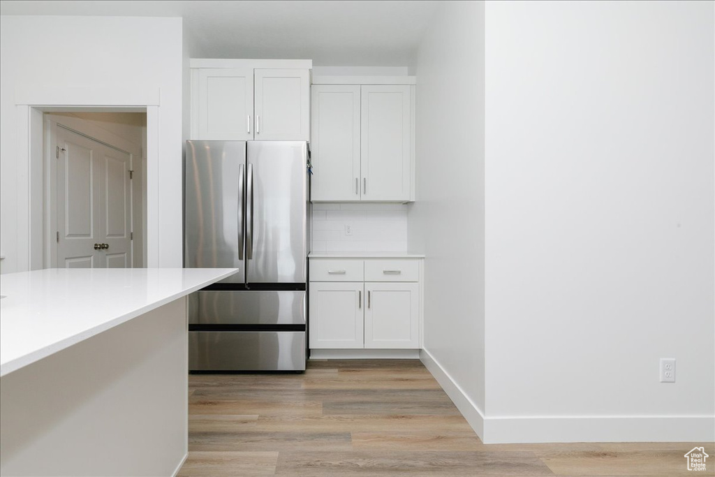 Kitchen with stainless steel refrigerator, light hardwood / wood-style flooring, white cabinets, and decorative backsplash