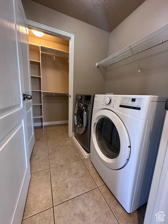 Laundry room with light tile patterned flooring, washer and clothes dryer, and a textured ceiling