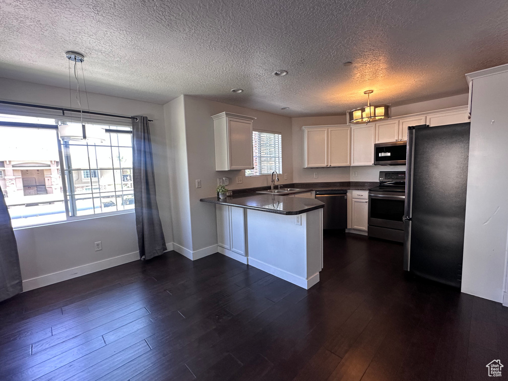 Kitchen with appliances with stainless steel finishes, a peninsula, a textured ceiling, white cabinets, and dark countertops
