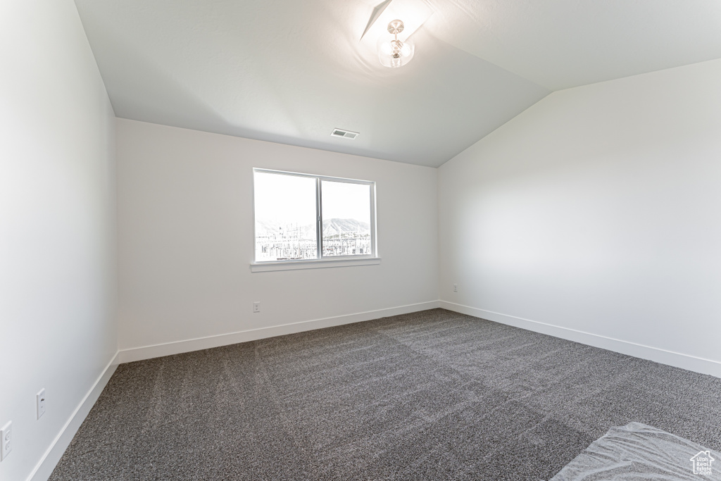 Spare room featuring lofted ceiling, dark carpet, and baseboards