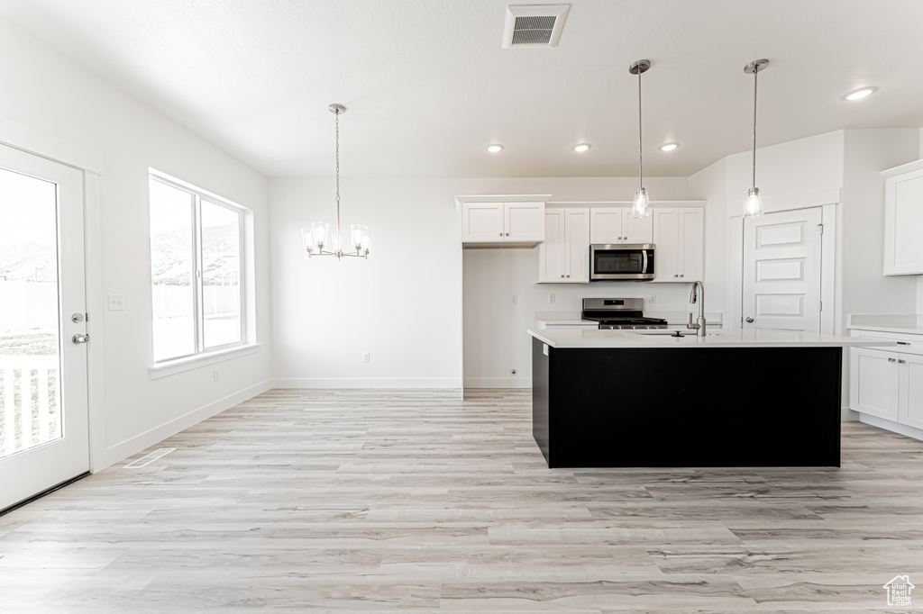Kitchen with stainless steel appliances, a chandelier, light countertops, white cabinets, and light wood-style floors