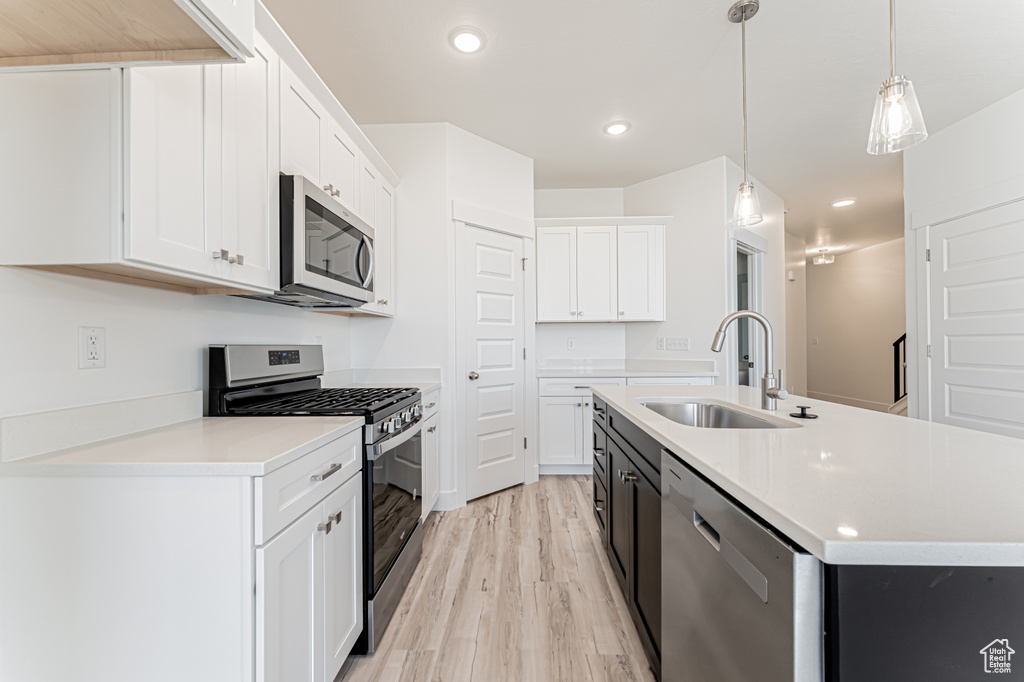 Kitchen featuring stainless steel appliances, a sink, light wood-style floors, white cabinets, and a center island with sink