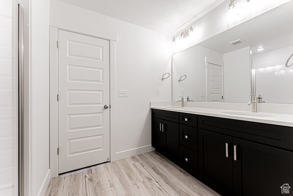 Bathroom with double vanity, baseboards, wood finished floors, and a textured ceiling