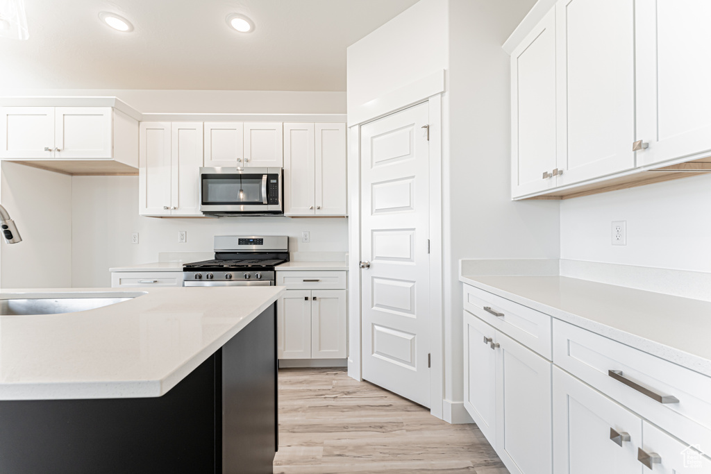 Kitchen featuring appliances with stainless steel finishes, light wood finished floors, light countertops, recessed lighting, and white cabinetry