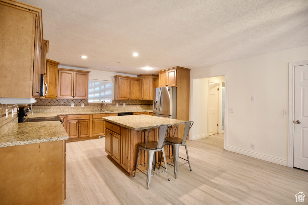 Kitchen featuring appliances with stainless steel finishes, a sink, a center island, backsplash, and a breakfast bar