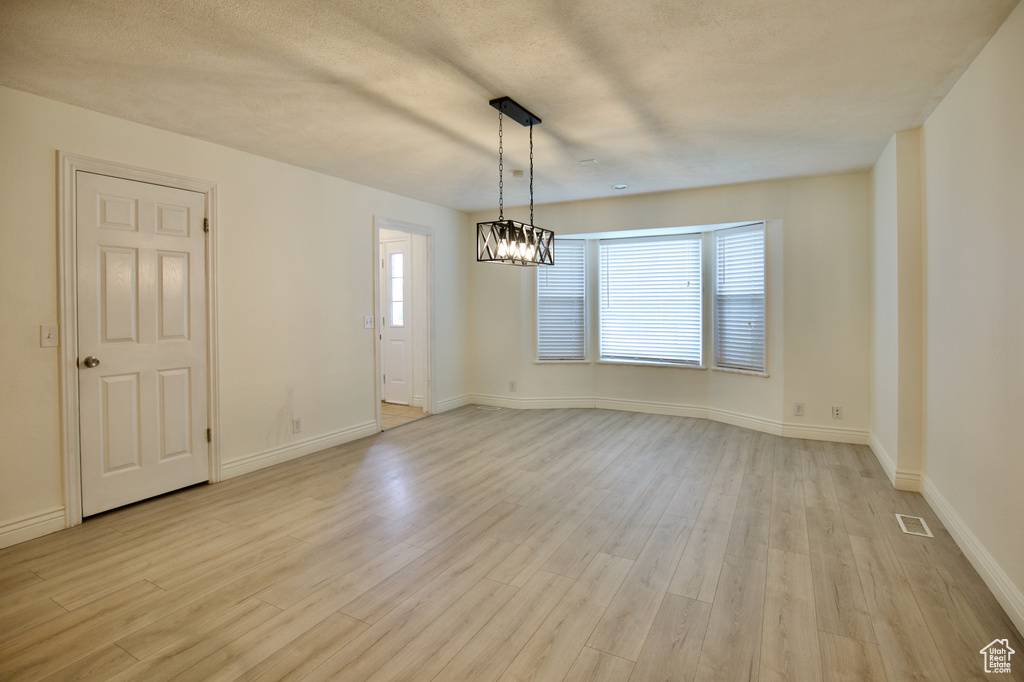 Spare room with light wood finished floors, a chandelier, and baseboards