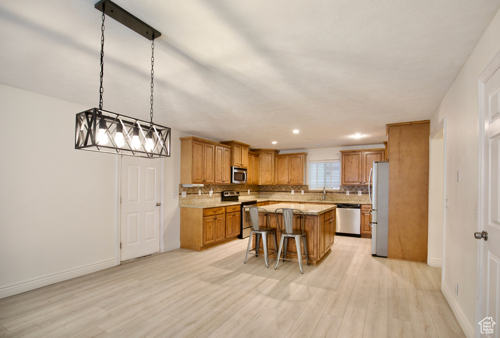 Kitchen featuring stainless steel appliances, a kitchen bar, light wood-style floors, decorative backsplash, and a center island