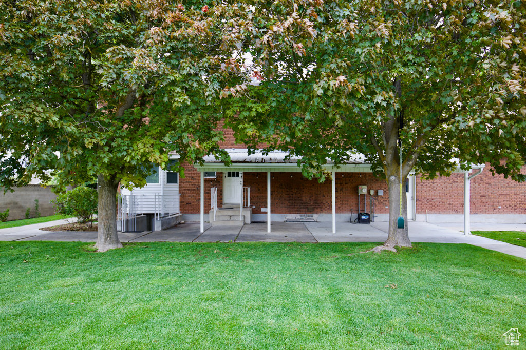 Obstructed view of property featuring brick siding, a front yard, and a patio