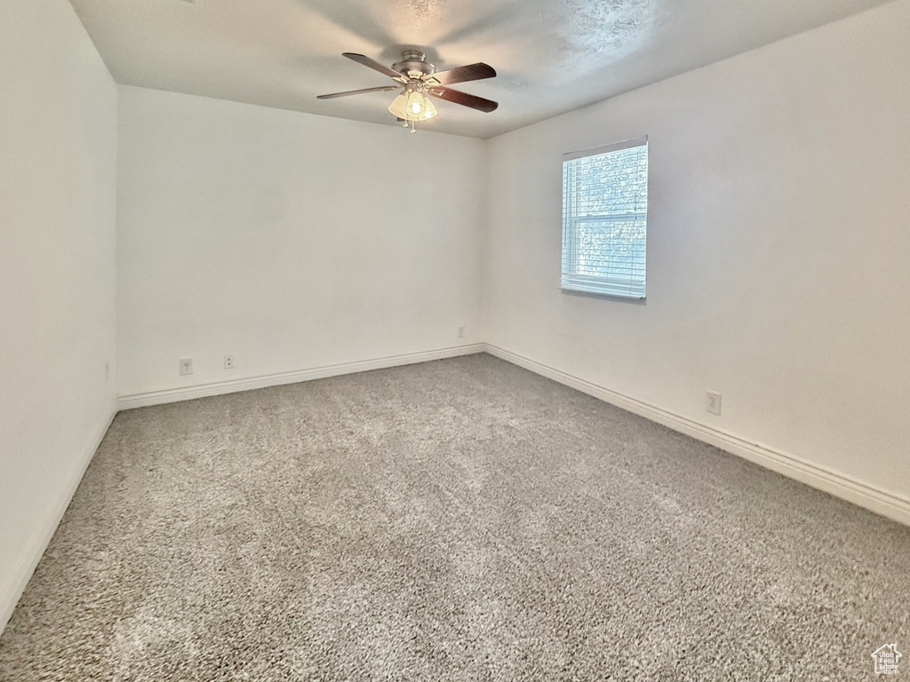 Carpeted spare room featuring ceiling fan and baseboards