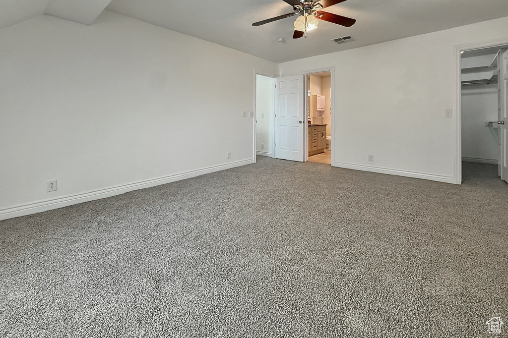 Unfurnished bedroom featuring a walk in closet, a wall unit AC, a closet, a ceiling fan, and connected bathroom