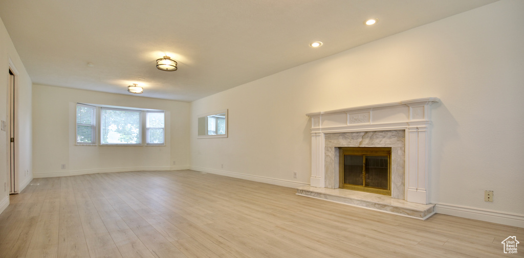 Unfurnished living room with light wood-type flooring, a high end fireplace, baseboards, and recessed lighting
