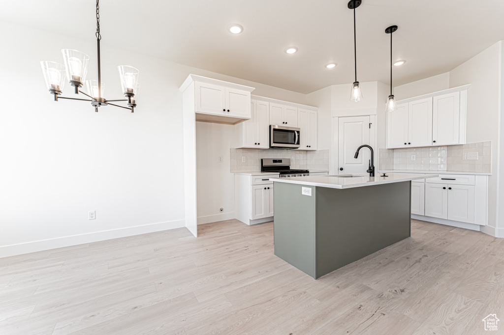 Kitchen with appliances with stainless steel finishes, a sink, a chandelier, light countertops, and light wood-type flooring