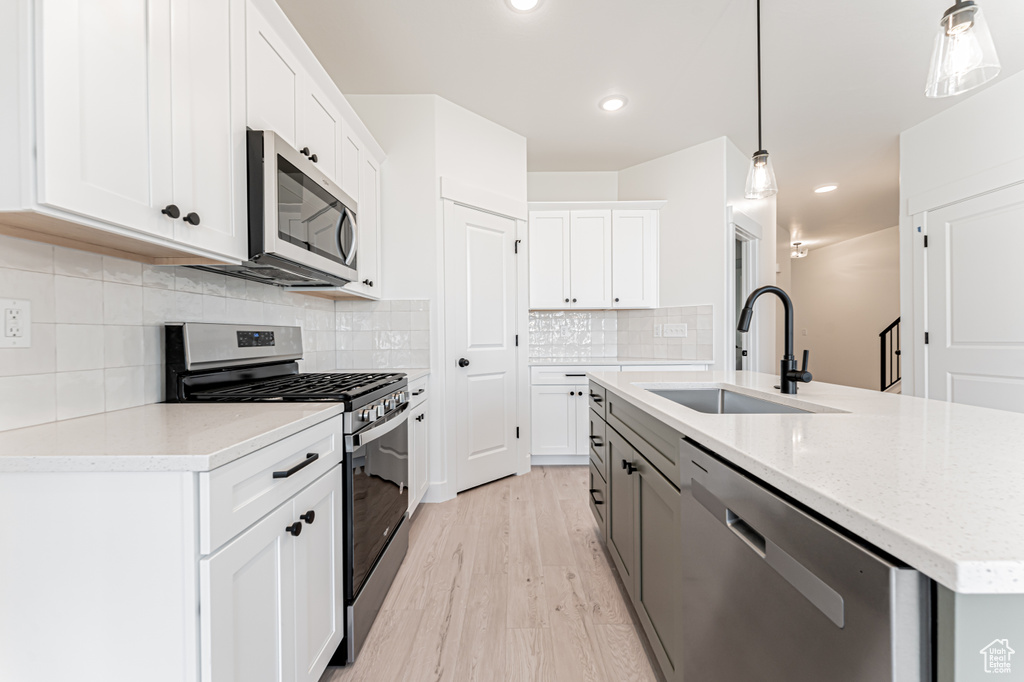 Kitchen with appliances with stainless steel finishes, a sink, an island with sink, light wood-type flooring, and white cabinets
