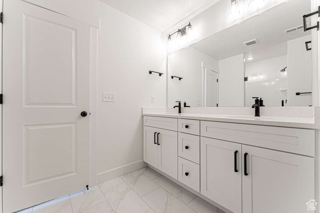 Bathroom with double vanity, marble look tile flooring, baseboards, and a shower stall