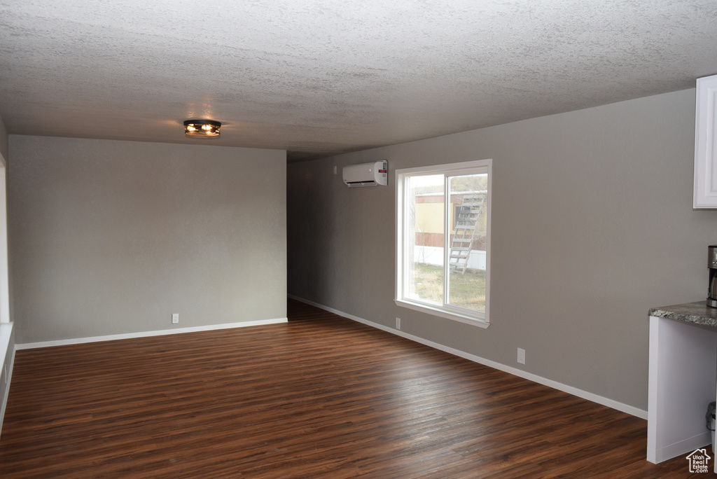 Interior space featuring dark wood-type flooring, a wall unit AC, a textured ceiling, and baseboards