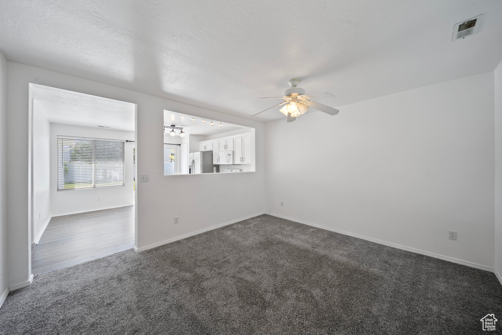 Unfurnished room with baseboards, ceiling fan, dark colored carpet, and visible vents