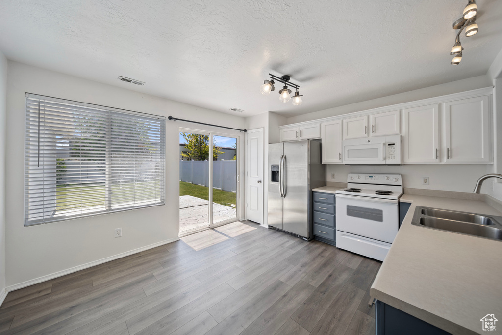 Kitchen featuring track lighting, white appliances, a textured ceiling, white cabinets, and a sink