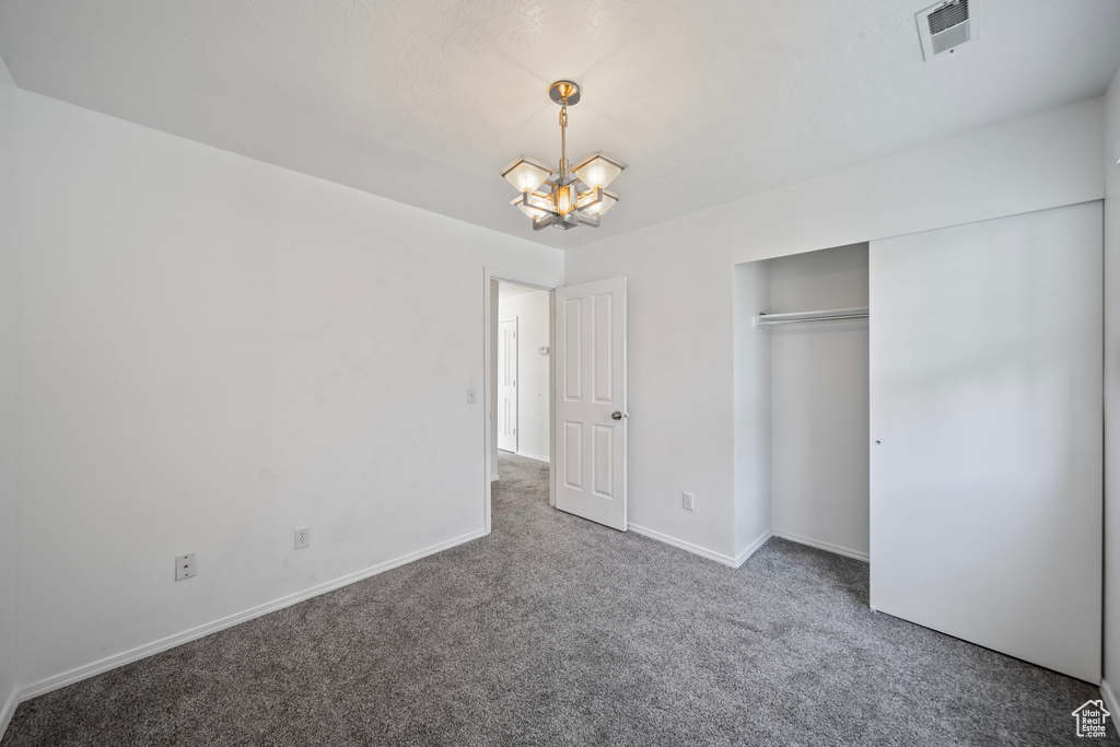 Unfurnished bedroom featuring carpet flooring, a notable chandelier, baseboards, visible vents, and a closet