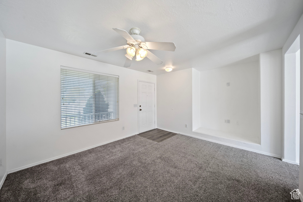 Unfurnished room with baseboards, ceiling fan, dark carpet, and visible vents