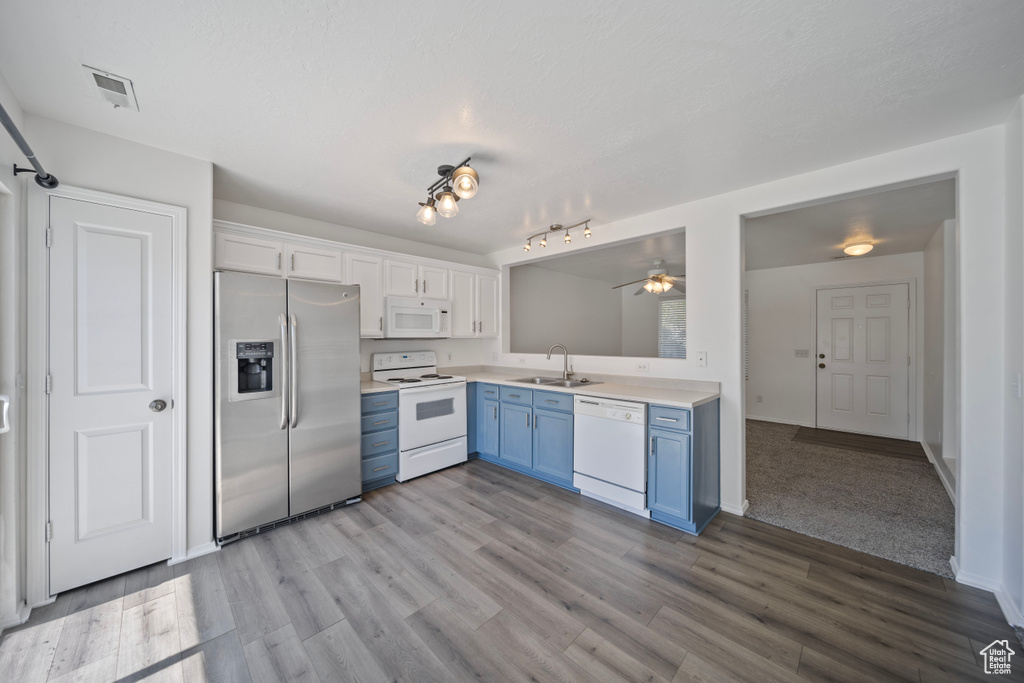 Kitchen featuring blue cabinetry, wood finished floors, a sink, light countertops, and white appliances