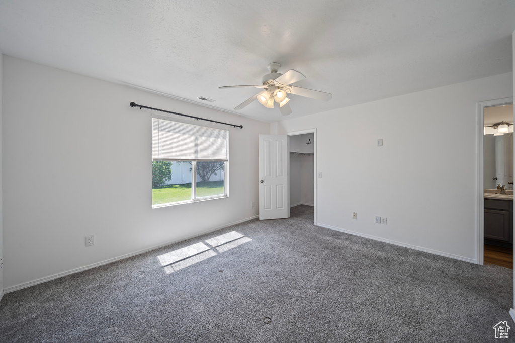 Unfurnished bedroom featuring a walk in closet, ceiling fan, carpet floors, baseboards, and connected bathroom