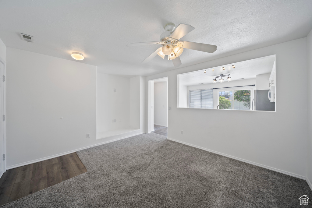 Carpeted spare room with visible vents, a ceiling fan, baseboards, and wood finished floors
