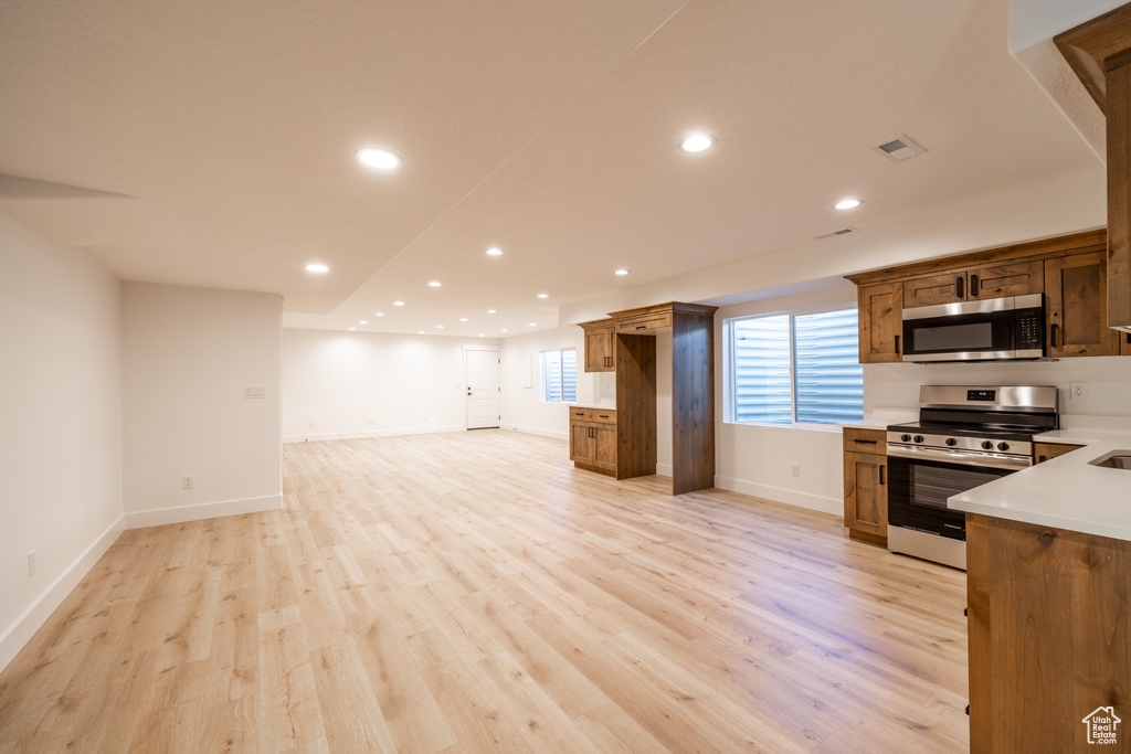 Kitchen with stainless steel appliances, open floor plan, light wood-style floors, light countertops, and recessed lighting