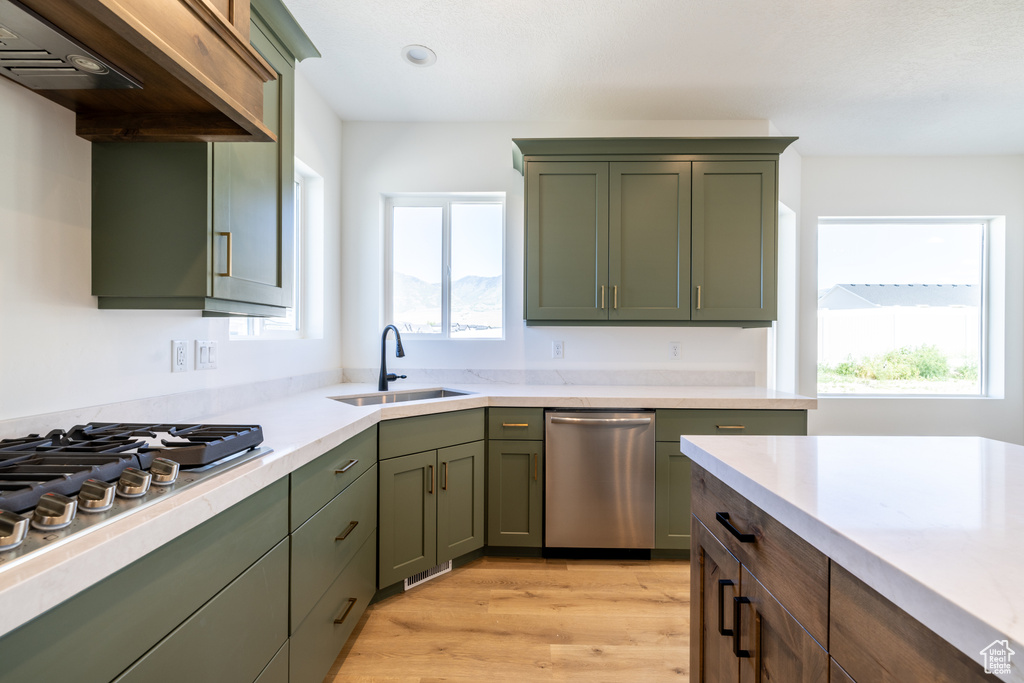Kitchen featuring appliances with stainless steel finishes, green cabinets, under cabinet range hood, light countertops, and healthy amount of natural light
